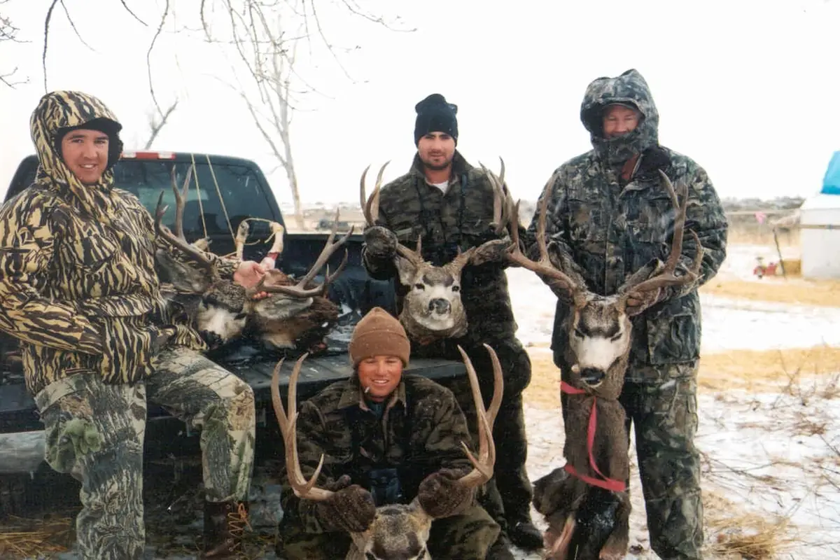 Four hunters in camouflage kneeling with their mule deer bucks at Charles M. Russell National Wildlife Refuge, Montana